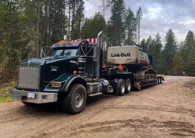 Skemxist Solutions Equipment Heavy Haul Truck Low Bedding a Power Clam Hydraulic Log Loader Into the Bush